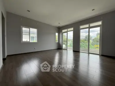 Spacious empty living room with large windows and wooden flooring, offering abundant natural light and garden view.