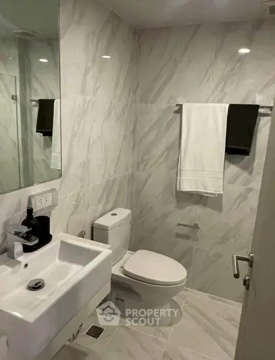 Modern bathroom with sleek fixtures and marble tiles, featuring a sink, toilet, and towel rack.