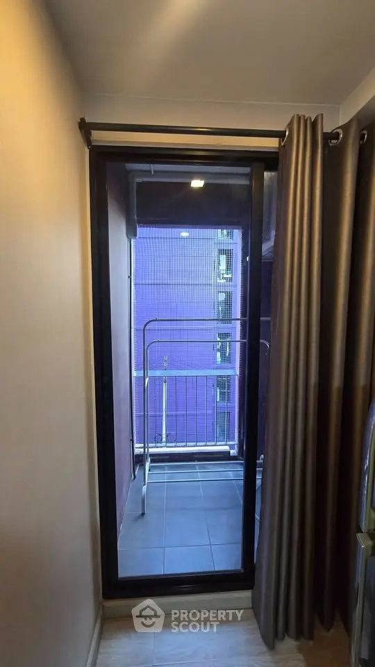 Modern apartment balcony with sliding glass door and curtain, offering a cozy outdoor space.