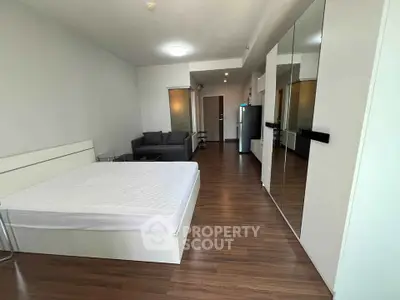 Spacious modern bedroom with sleek wooden flooring and mirrored wardrobe in a stylish apartment.