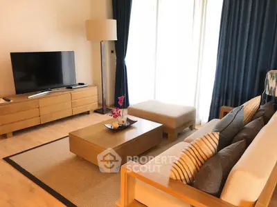 Modern living room with stylish furniture and large TV, featuring natural light and elegant decor.