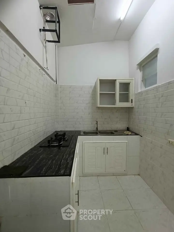 Compact kitchen with sleek black countertop and white cabinetry in modern apartment.