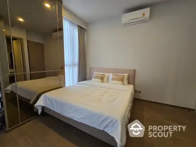 Spacious bedroom with polished wooden flooring, large mirrored wardrobe, and modern air conditioning unit, bathed in natural light from the window.