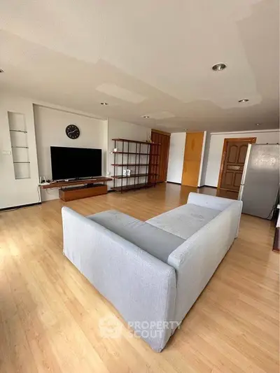 Spacious living room with modern decor and wooden flooring, featuring a large TV and comfortable sofa.
