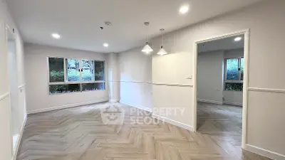 Spacious empty room with elegant herringbone flooring and large windows.