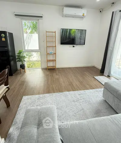 Modern living room with sleek wooden flooring, stylish furniture, and a wall-mounted TV for a cozy ambiance.
