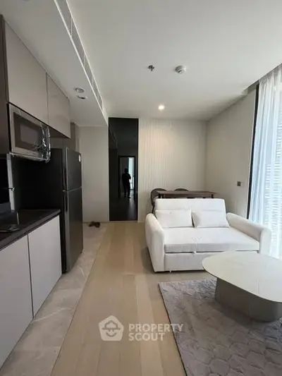 Modern living room with sleek kitchen, featuring a cozy sofa and stylish decor in a contemporary apartment.