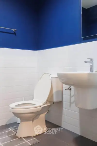 Modern bathroom with blue and white tiles, featuring a sleek toilet and wall-mounted sink.