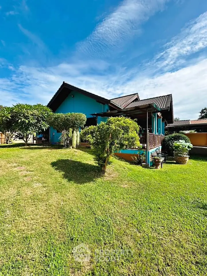 Charming blue house with lush garden and spacious lawn under a clear blue sky.