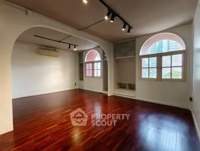 Spacious living room with hardwood floors and arched windows in a modern apartment.