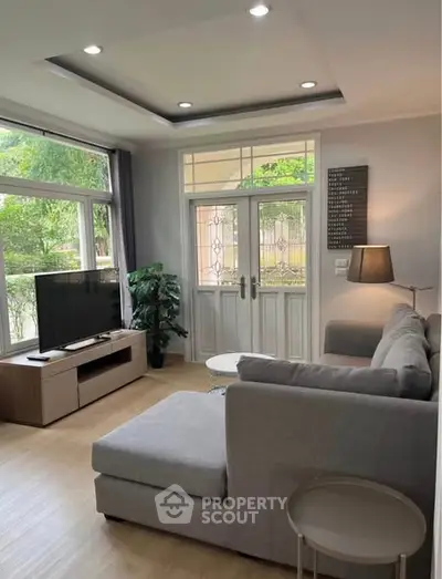 Modern living room with large windows, stylish gray sofa, and flat-screen TV, offering a cozy and inviting atmosphere.