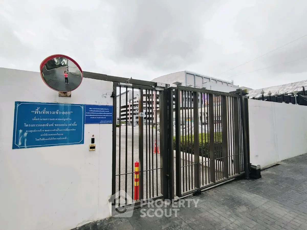 Secure gated entrance of modern residential complex with ample parking space.