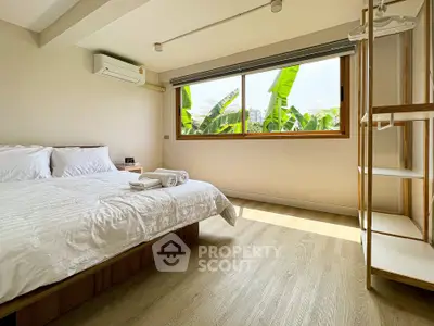 Bright bedroom with large window and modern decor, featuring a cozy bed and lush greenery view.