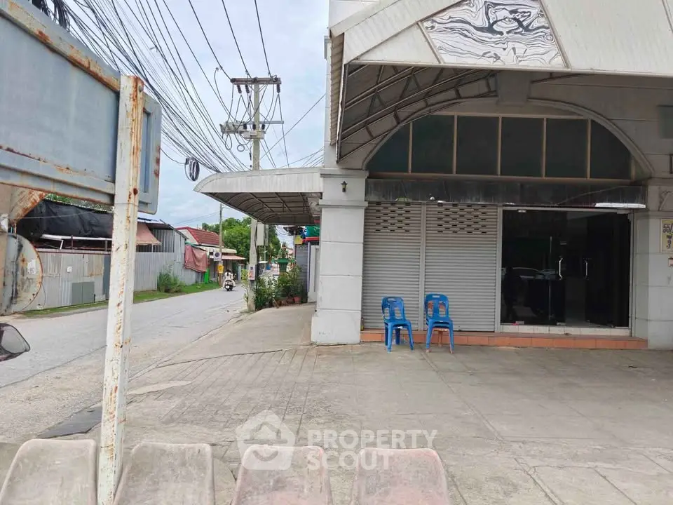 Street view of commercial property with closed shutters and two blue chairs outside.
