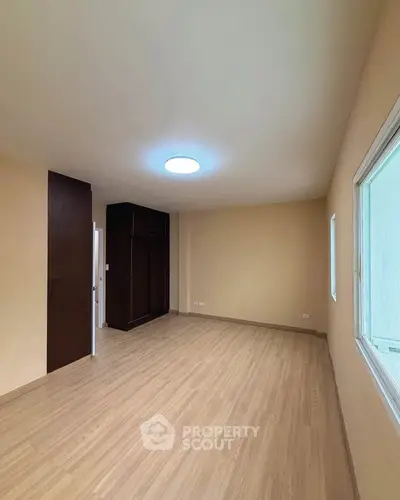 Spacious empty room with wooden flooring and large window, ideal for customization.