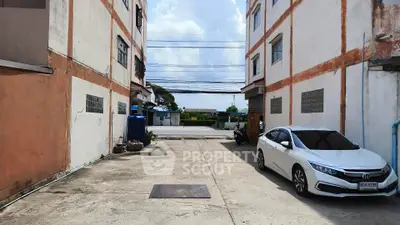 Spacious parking area between two residential buildings with a parked car and clear sky view.