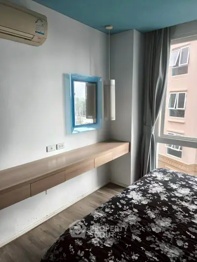 Modern bedroom with floral bedding, wall-mounted desk, and large window with city view.