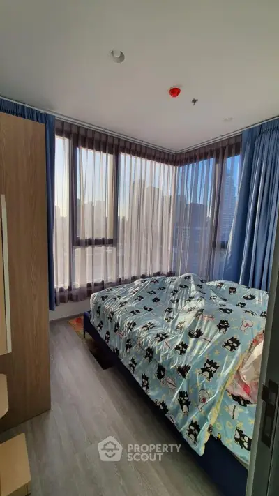 Cozy bedroom with large windows and city view, featuring stylish curtains and modern decor.