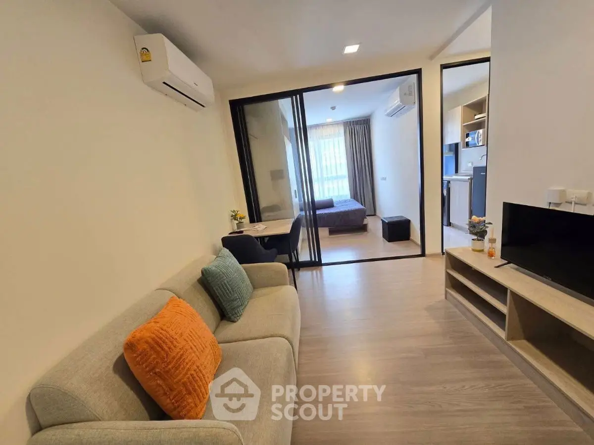 Modern open-plan living room with cozy sofa and view into bedroom