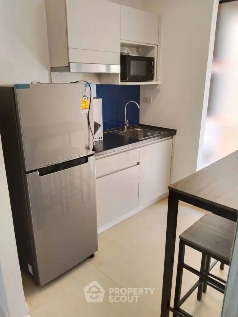 Modern compact kitchen with stainless steel fridge and microwave, sleek cabinetry, and breakfast bar.