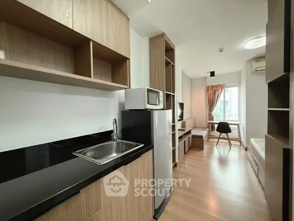 Modern studio apartment with sleek kitchen and cozy living area, featuring wood accents and natural light.