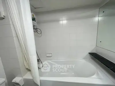 Modern bathroom with sleek white tiles and bathtub, featuring a wall-mounted shower and large mirror.
