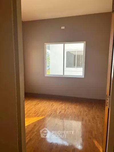 Spacious empty room with wooden flooring and large window, perfect for customization.