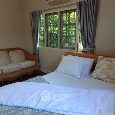 Cozy bedroom with natural light and garden view, featuring a comfortable bed and stylish wicker seating.