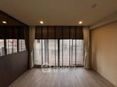 Spacious living room with large windows and elegant blinds, perfect for natural light.