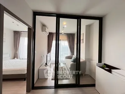 Modern apartment with glass partition separating living room and bedroom, featuring sleek furniture and natural light.