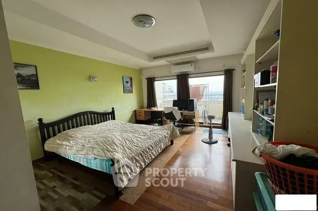 Spacious bedroom with balcony and city view, featuring wooden flooring and modern decor.