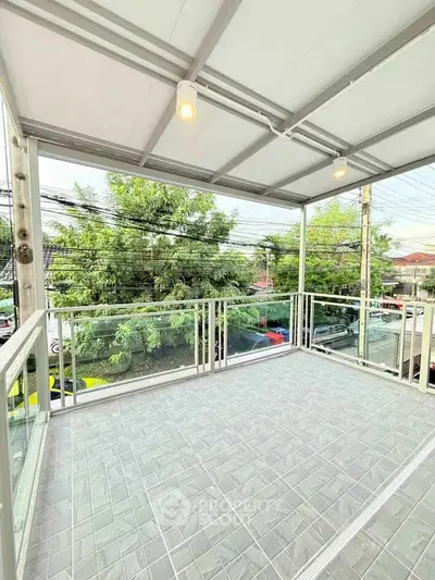 Spacious balcony with modern railing and tiled floor overlooking lush greenery.