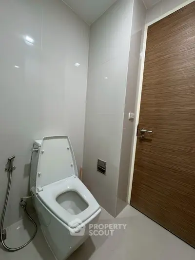 Modern bathroom with sleek toilet and wooden door, featuring minimalist design and clean lines.