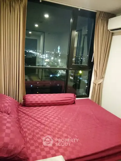 Cozy bedroom with city view from large window, featuring elegant red bedding and modern air conditioning.