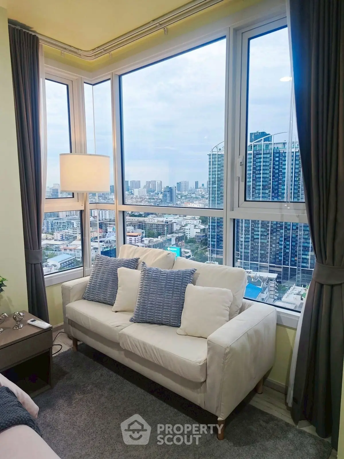 Modern living room with stunning city view from large windows, cozy white sofa and elegant decor.