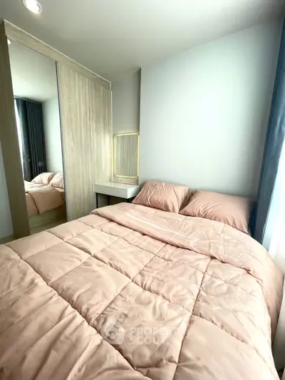 Cozy bedroom with soft pink bedding and mirrored wardrobe in modern apartment.