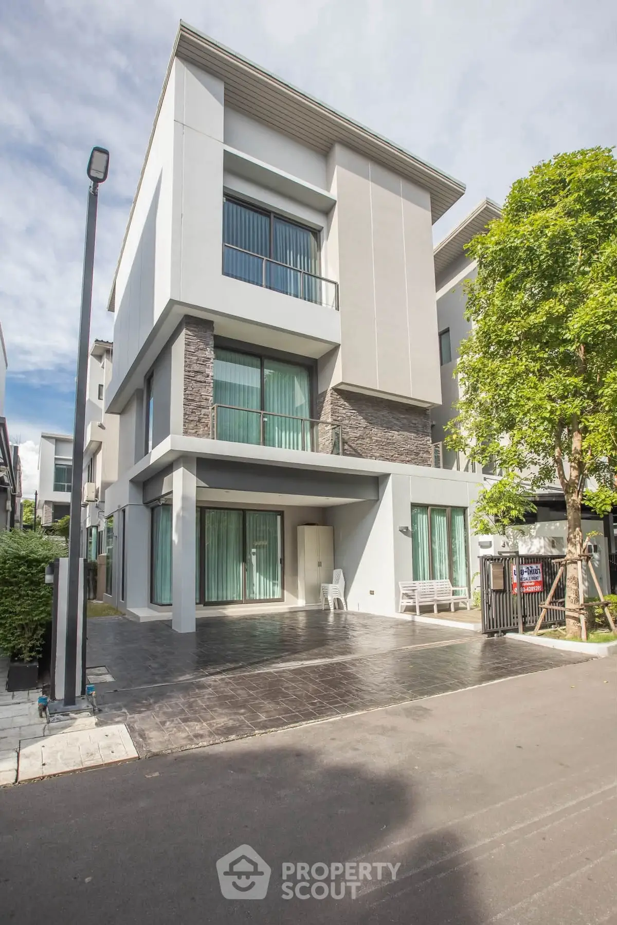 Modern three-story house with large windows and sleek design in a suburban neighborhood.