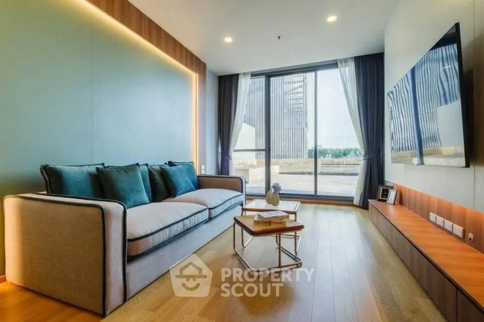 Modern living room with large sofa, wall-mounted TV, and floor-to-ceiling windows offering a stunning view.