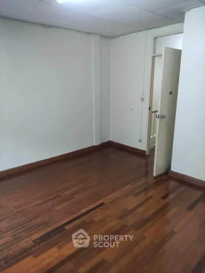 Spacious empty room with wooden flooring and open door, ideal for customization.