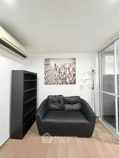 Modern living room with black leather sofa, bookshelf, and cityscape artwork, featuring sleek design and natural light.