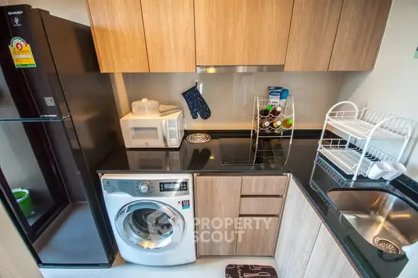 Modern kitchen with sleek appliances and wooden cabinetry, featuring a washing machine and microwave.