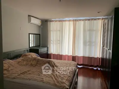 Cozy bedroom with large windows and wooden flooring, featuring a modern air conditioning unit.
