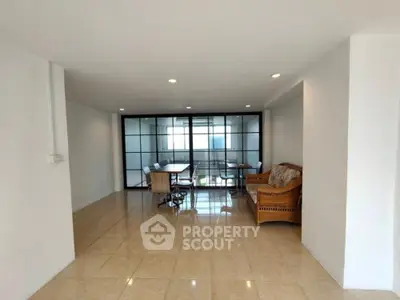 Spacious and sunlit living room with gleaming tiled floors, leading to a cozy balcony with a serene view, perfect for urban living.