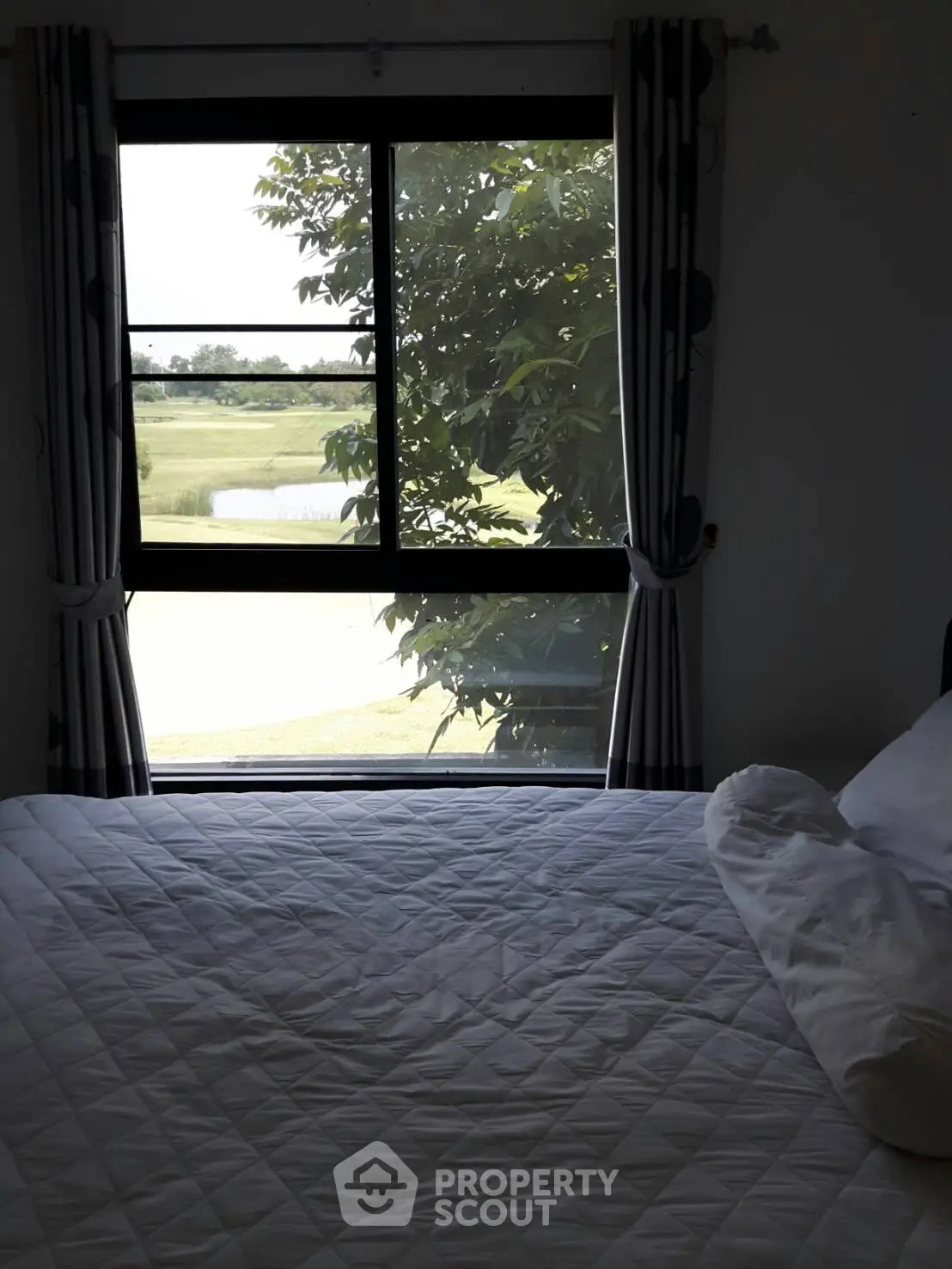Cozy bedroom with scenic window view of lush greenery and golf course.