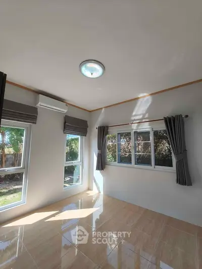 Bright room with large windows and garden view, featuring tiled flooring and modern curtains.