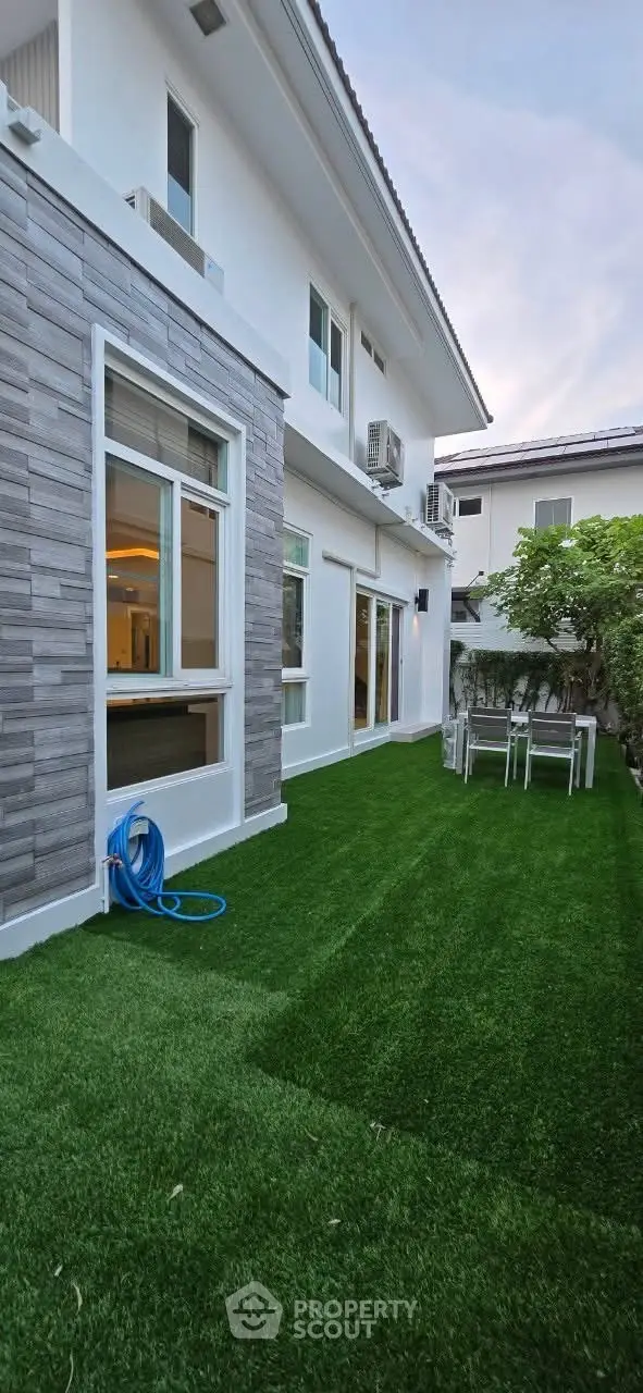Charming modern house exterior with lush green lawn and stylish patio furniture.