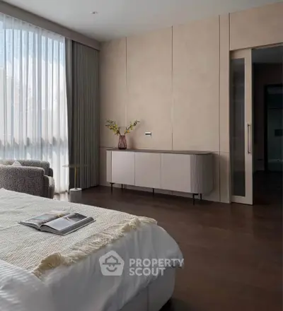 Elegant bedroom with modern decor, featuring a cozy bed, stylish sideboard, and large window with sheer curtains.