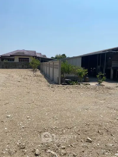 Spacious plot with potential for development, featuring a fenced area and nearby residential building.