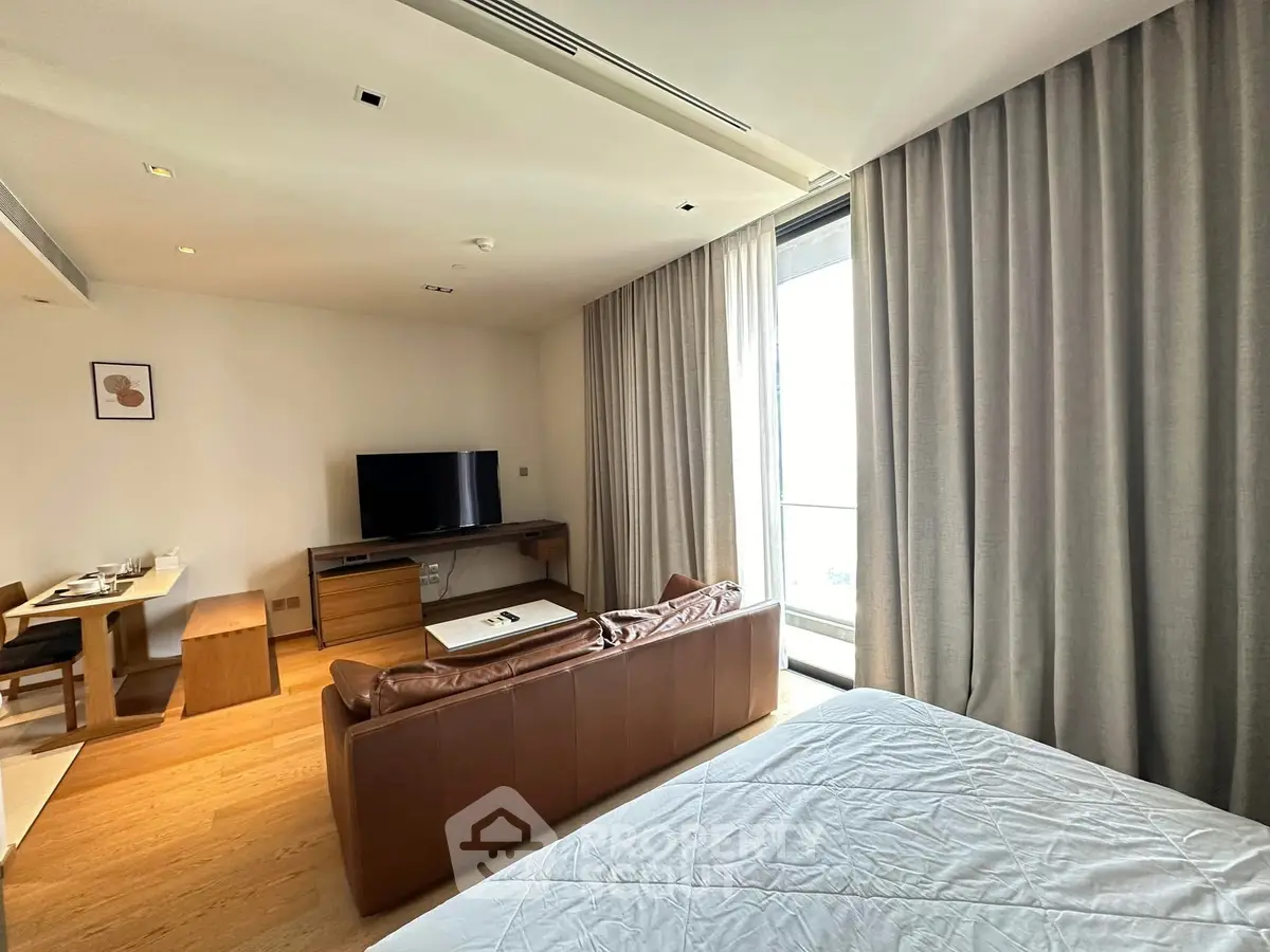 Modern living room with leather sofa, TV, and dining area in a bright apartment.