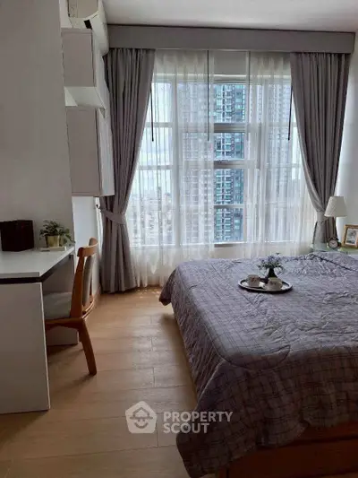 Cozy bedroom with large window offering city view, featuring a study desk and elegant decor.